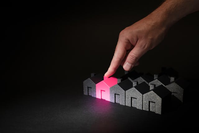 a finger pointing to a red house amidst a number of black ones