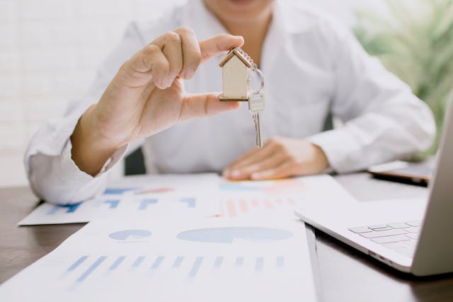 a person holding a house figurine and key with documents around them